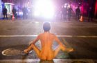 A naked protester sits in front of police
